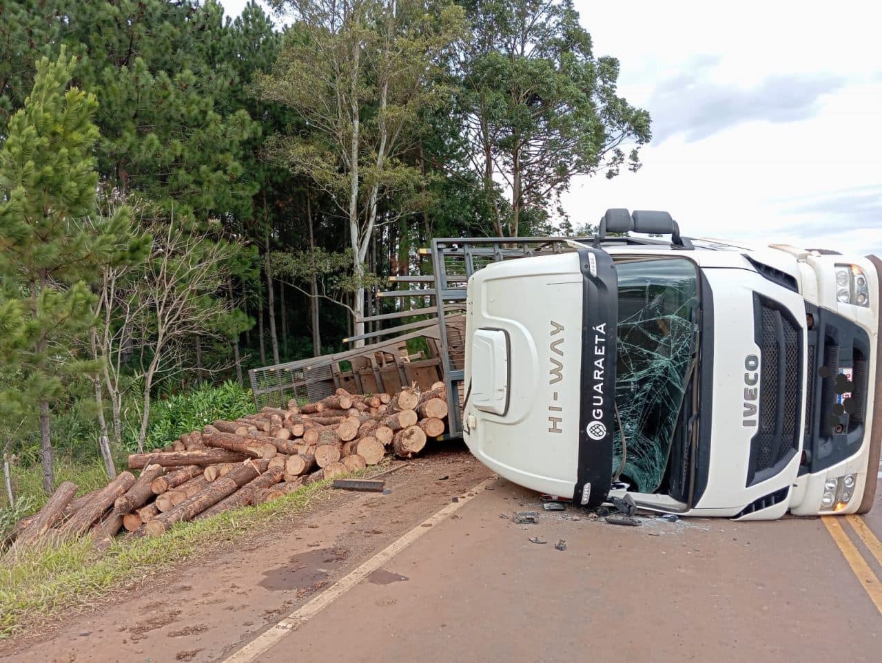 Motorista pula da cabine antes de carreta carregada de toras de madeira tombar na SC-160