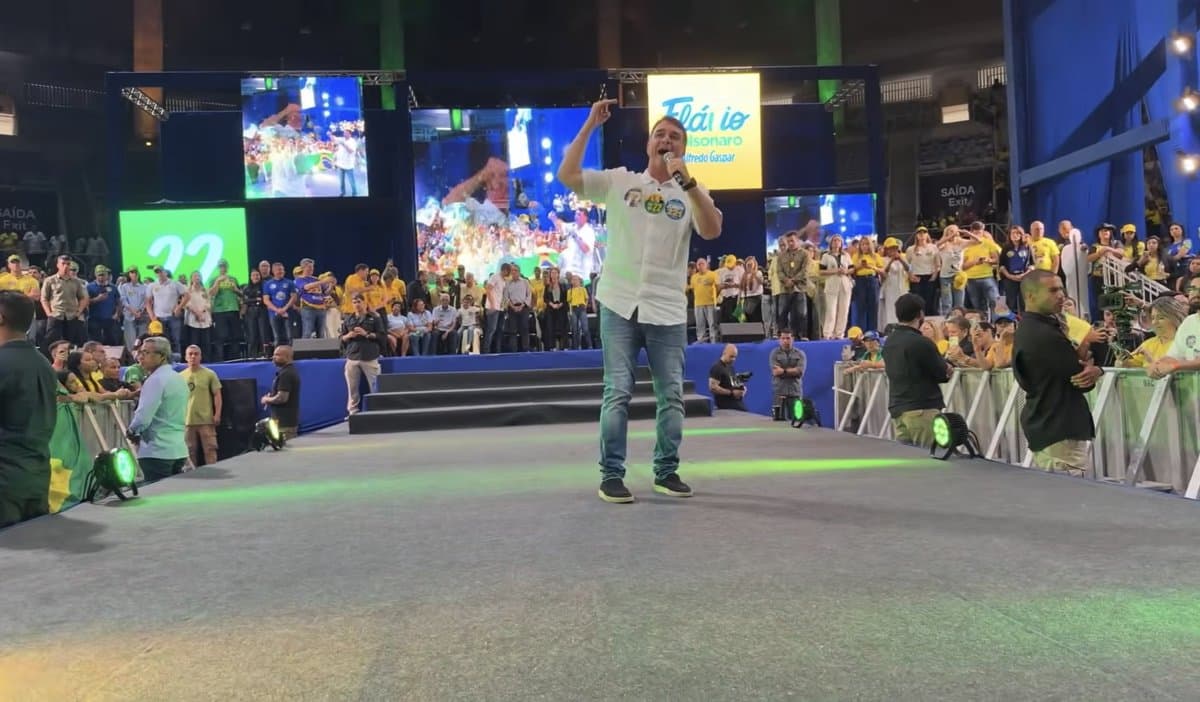 Flavio Bolsonaro discursa com microfone em cima do palco durante evento de campanha em ginasio lotado