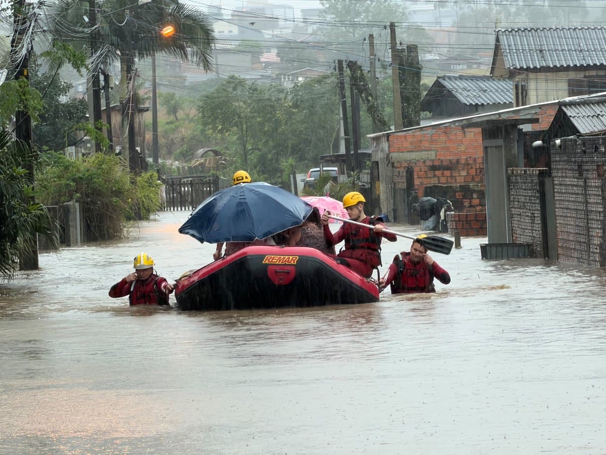 Bombeiros conduzem bote com moradores por rua alagada no bairro Paraíso, em Criciúma