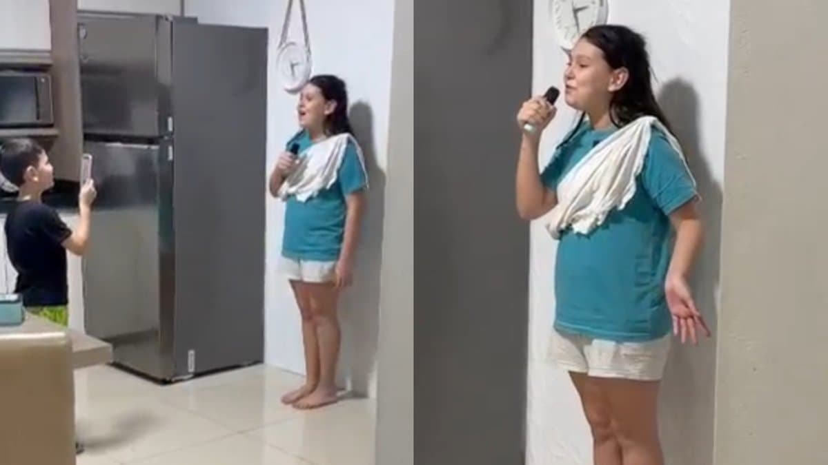 Menina com toalha no peito como faixa presidencial discursa na cozinha enquanto menino filma com celular